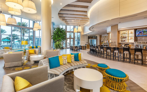 Grey sofa with wicker seating & colorful pillows next to bar with stools