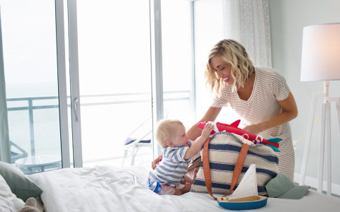 Woman packing things into striped bag with baby on bed
