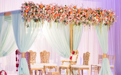 Gold chairs on stage with white canopy and rose decor
