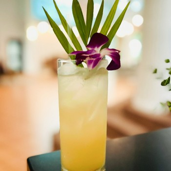 yellow cocktail with purple flower and green leaf