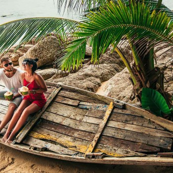 man and woman drinking from coconuts on wooden boat