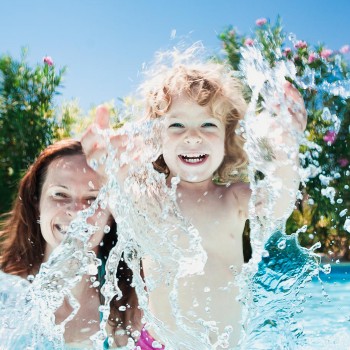 little boy splashing in the water with his mom behind him