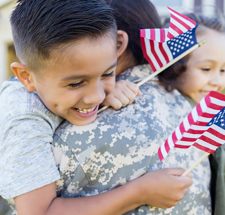 Young boy hugging is military mom with little American flags 