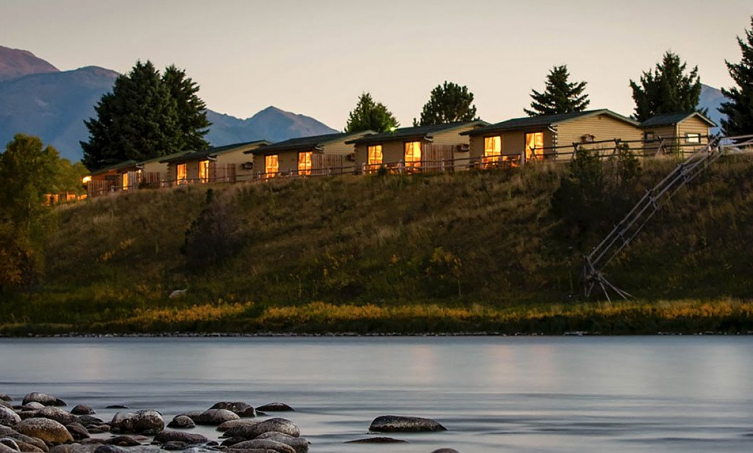 Row of cabins on top of a hill in the mountains behind a river