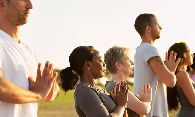 Row of five people with their eyes closed and hands placed together practicing yoga