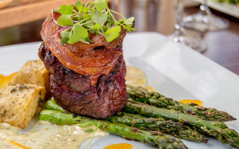 Plate of steak topped with bacon with potatoes and asparagus 
