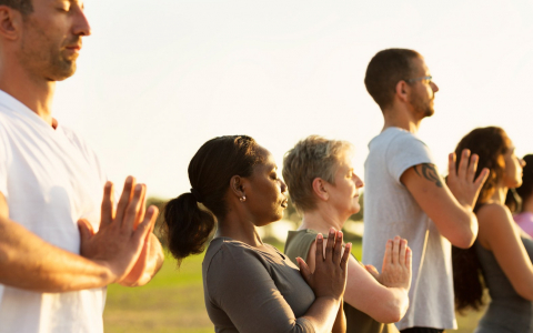 Row of five people with their eyes closed and hands placed together practicing yoga
