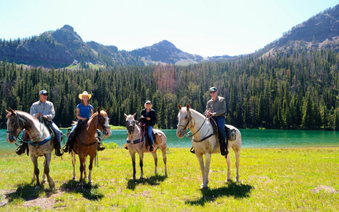 Four people atop horses in front of a lake in the mountains