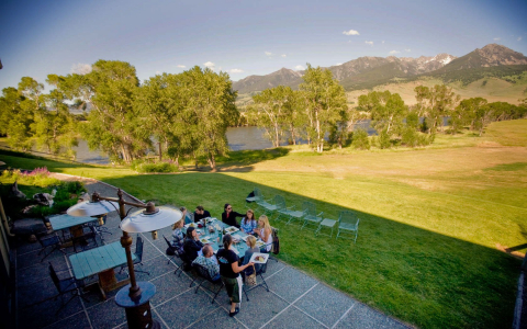Outdoor dining patio overlooking a large field, lake and mountains