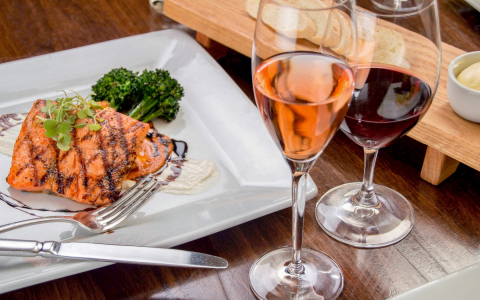 Plate of grilled salmon and broccoli with two glasses of wine