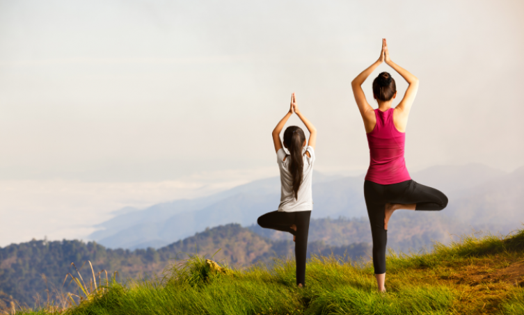 mother and daughter doing yoga on a hill top