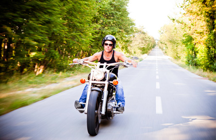 Man riding motorcycle down street surrounded by trees