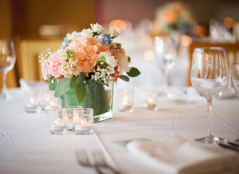 Table set up for a wedding ceremony with white linens, wine glasses, mini candles and a floral center piece