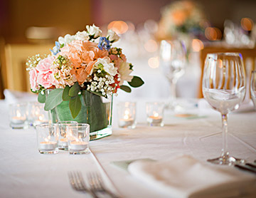 Table set up for a wedding ceremony with white linens, wine glasses, mini candles and a floral center piece