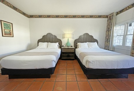 Two queen beds with lamp and window with open curtains