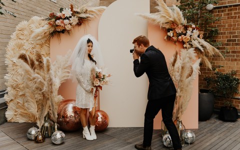 groom taking a close up picture of the bride next to a photo backdrop set-up