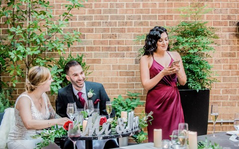 bridesmaid standing up while on her phone and bride and groom are sitting next to her 