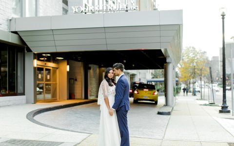 couple on the day of their wedding holding hands and facing each other in front of hotel entrance