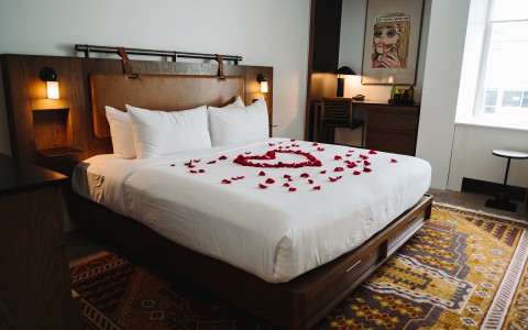 guestroom with king bed covered in rose petals in the shape of a large heart