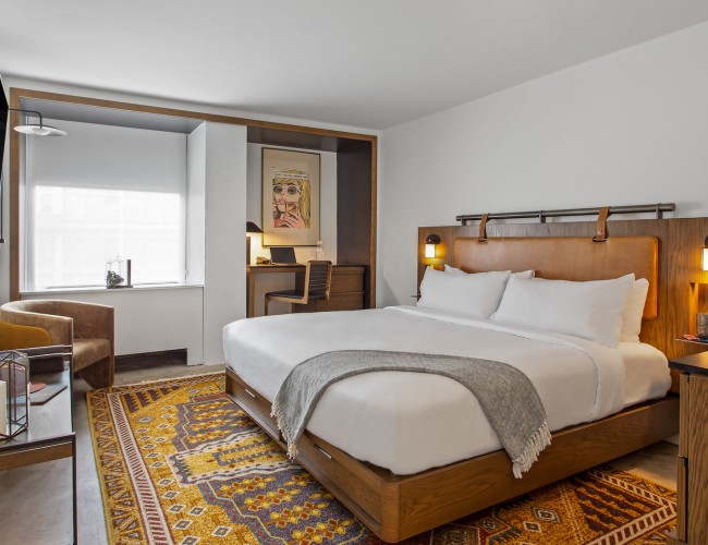 premium king room with yellow and blue abstract carpet below wooden bed frame and bed with crisp white sheets and pillows