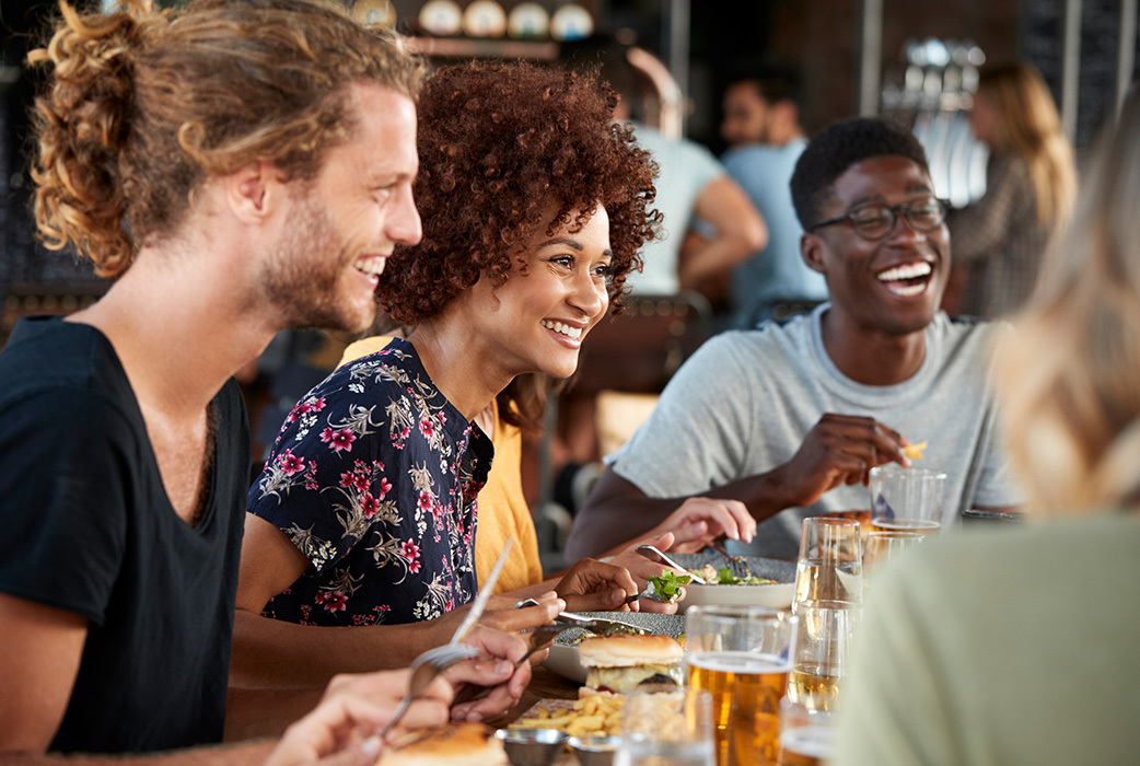 group of friends laughing around lunch table with food and drinks