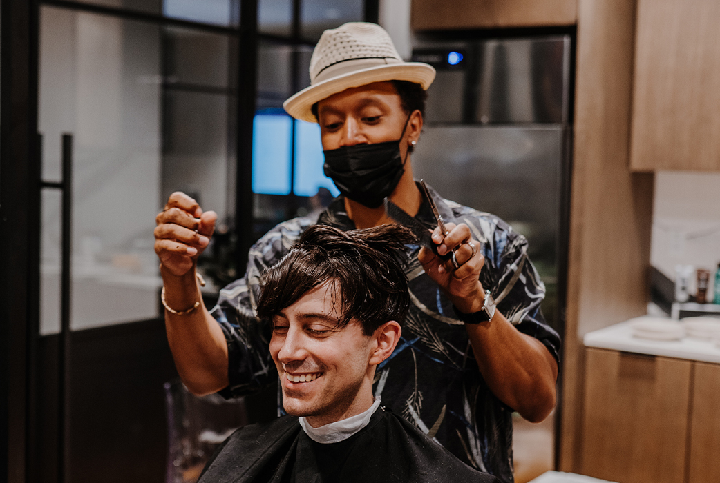 Smiling man getting his hair cut by hairdresser with a cool hat on